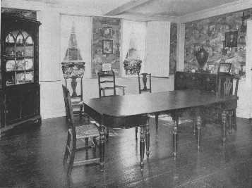 The warm tones of a brown Chinese wallpaper are
 attractive with the mahogany furniture, and the pattern is prevented
from becoming monotonous by the strong rectangular lines of the ivory
woodwork which frames it. The corner cupboard and the exceptionally fine
dining-table and the variety of chairs are interesting.