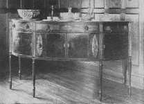 This fine Sheraton sideboard shows curved doors, and
knife boxes with oval inlay of satinwood. The center cupboard is
straight. The legs are reeded.