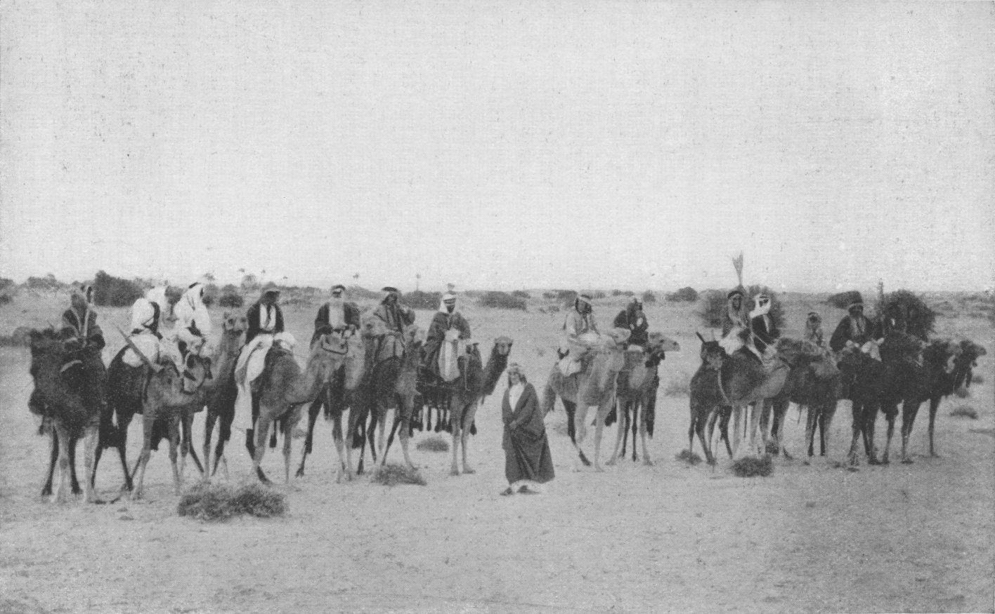Photo wide shot of Lawrence standing in a line of
                Arabs on camels