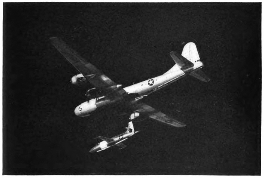 A small airplane flying directly under a larger plane