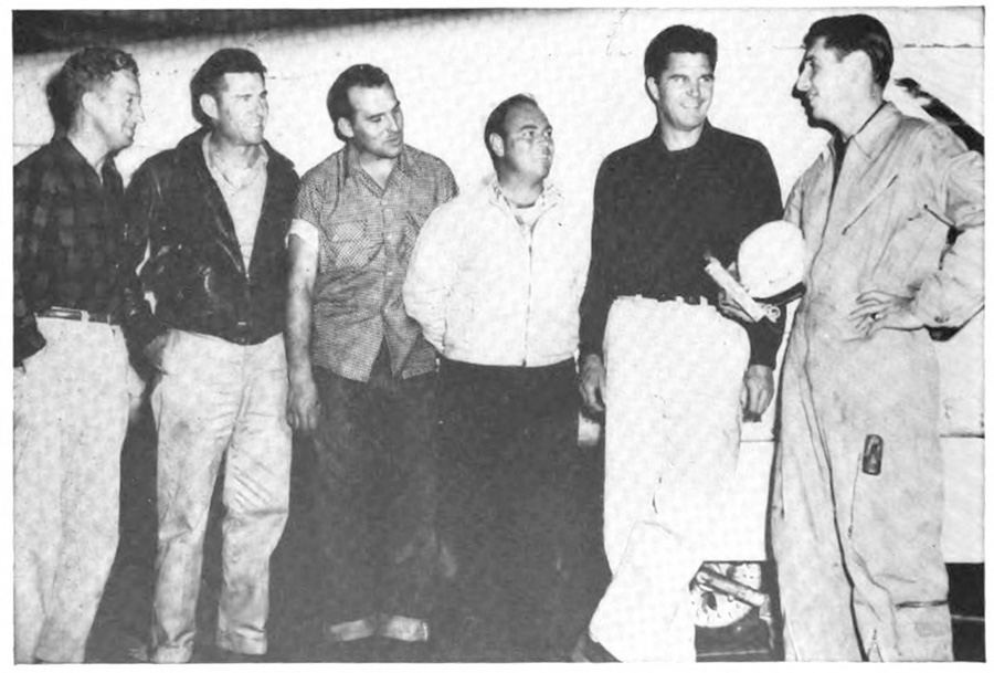 Five men standing next to a man in a flight suit